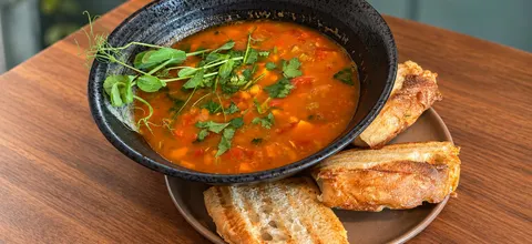 Marokkansk suppe med kikerter og kylling i en svart skål, toppet med urter og servert med ristet brød
