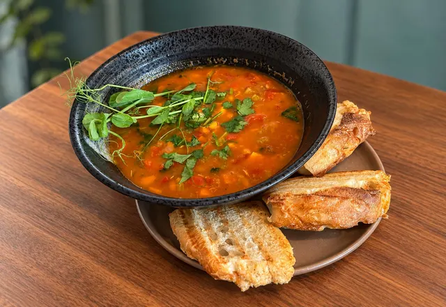 Marokkansk suppe med kikerter og kylling i en svart skål, toppet med urter og servert med ristet brød