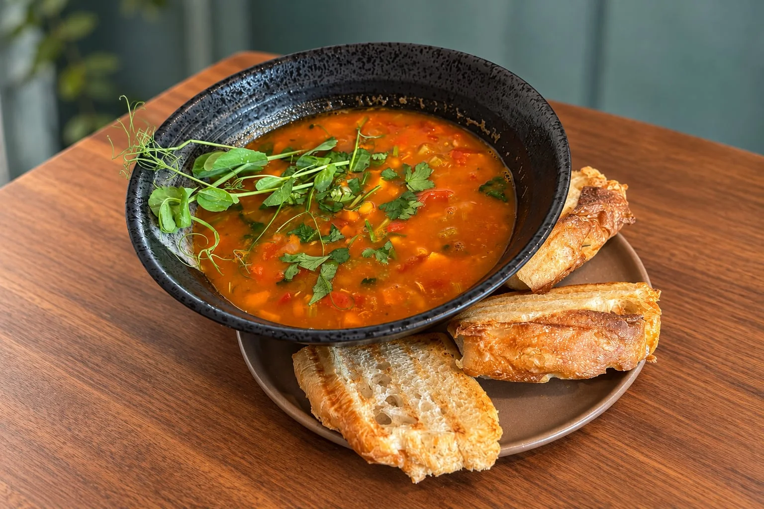 Marokkansk suppe med kikerter og kylling i en svart skål, toppet med urter og servert med ristet brød