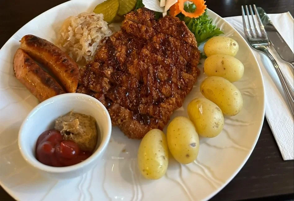 Wienerschnitzel og to bratwurst med surkål, kokte poteter, sylteagurk, ketsjup og sennep på en hvit tallerken
