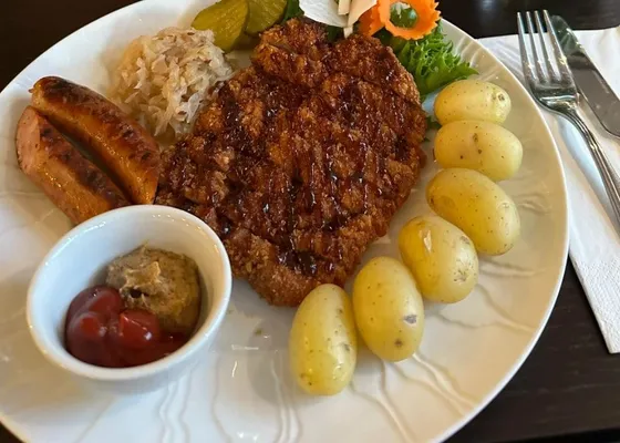 Wienerschnitzel og to bratwurst med surkål, kokte poteter, sylteagurk, ketsjup og sennep på en hvit tallerken