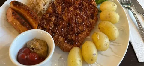 Wienerschnitzel og to bratwurst med surkål, kokte poteter, sylteagurk, ketsjup og sennep på en hvit tallerken